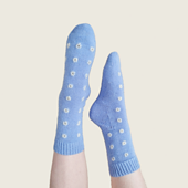 Cornflower blue socks on feet with white embroidered eyelets in a grid pattern. The feet are pointed in the air against a beige background.