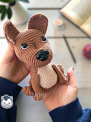 Crochet Amigurumi pattern of a brown and beige American Staffordshire dog sitting on a white wooden surface, perfect for an instant download pattern.