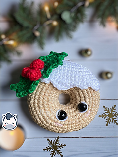 Crochet amigurumi pattern of two Christmas donuts: one beige with white icing and holly, and one blue with a colorful string of Christmas lights