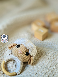 Crochet sheep baby rattle with white and beige amigurumi head on a natural wooden ring.