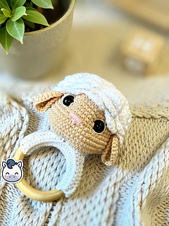 Crochet sheep baby rattle with white and beige amigurumi head on a natural wooden ring.