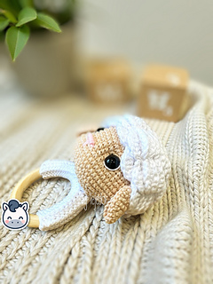Crochet sheep baby rattle with white and beige amigurumi head on a natural wooden ring.