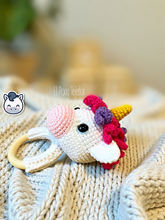 Crochet amigurumi pattern of a baby unicorn rattle with a golden horn, pink and purple mane on a wooden ring.