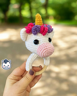 Crochet amigurumi pattern of a baby unicorn rattle with a golden horn, pink and purple mane on a wooden ring.