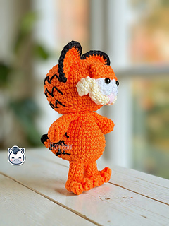 Crochet orange cat amigurumi inspired by Garfield, featuring rounded cheeks, embroidered details and black stripes on the back.