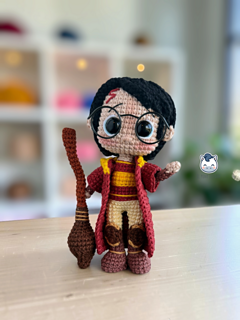 Two Harry Potter amigurumi dolls shown from the front on a wooden table. On the left, Harry wears a red and gold Quidditch uniform and holds a brown broom. On the right, he wears a black cloak, a red and gold scarf and a brown Sorting Hat. Both have black hair and round glasses. The El Pony Tejedor logo appears on the left.