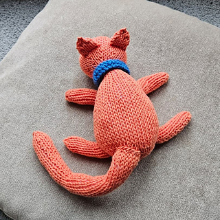 Ginger knitted cat with blue collar on cushion