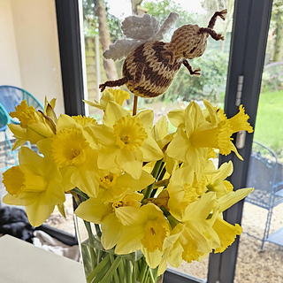 Flying knitted bee toy sitting in bunch of flowers