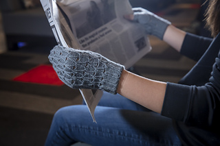A person holding a newspaper while wearing grey fingerless gloves. 