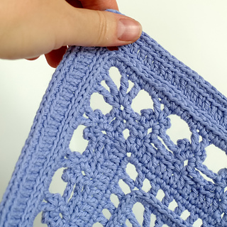 Corner detail of crochet lace pattern square with hand for scale