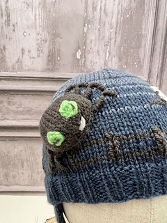 Close up of the knitted spider with green eyes on the blue striped spider hat, kids Halloween hat knitting pattern
