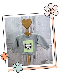 Woodland baby jumper with a knitted raccoon face, hanging on a wooden heart hanger, Bandit motif for babies and toddlers
