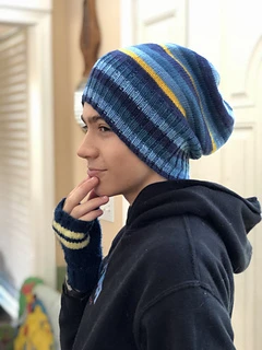 A teen boy looking left and holding his hand to his chin. He's wearing a blue hoodie and a blue and yellow striped slouchy hat.