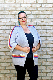 Curvy female with blue hair wearing a grey cardigan with accent purple, pink, orange, yellow and white puff stitches.