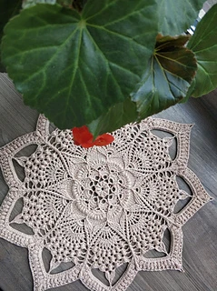 Finished Arabesque crochet doily displayed on a table, demonstrating its size and elegant pattern