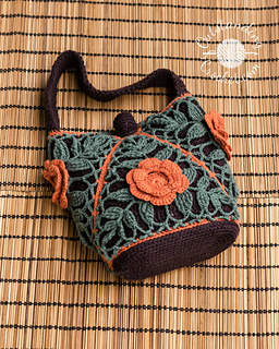 Small crochet purse composed of 4 joined-as-you-go triangular motifs. The design features sage green leaf lace patterns over a dark brown lining, trimmed with bright orange diagonal seams and a matching 3D crochet flower on the front. Features oval base and a handle.