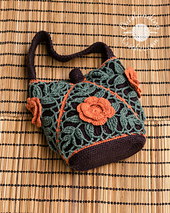 Small crochet purse composed of 4 joined-as-you-go triangular motifs. The design features sage green leaf lace patterns over a dark brown lining, trimmed with bright orange diagonal seams and a matching 3D crochet flower on the front. Features oval base and a handle.