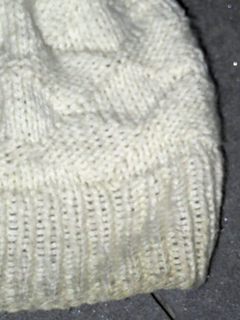 [Image Description: a close look at the ribbing and textured knit and purl pattern of a hat.  The ribbing is one by one ribbing, the hat is knit in a textured diamond pattern of knits and purls.]