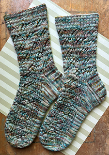 Image Description: a pair of ribbed lace socks laying flat. They are knit in a multicoloured variegated yarn and have a diagonal lace motif on the leg and the top of the foot