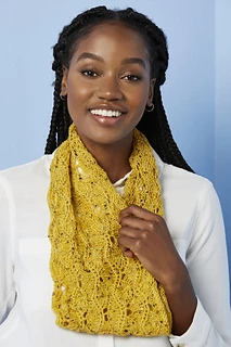 [Image Description: A woman wearing a knit lace cowl, in a scalloped lace pattern. The yarn is fingering-weight yarn in a mustard yellow colour with flecks of black.  The woman is holding one edge of the cowl.]