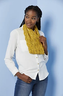 [Image Description: A woman wearing a knit lace cowl, in a scalloped lace pattern. The yarn is fingering-weight yarn in a mustard yellow colour with flecks of black.  The woman is holding one edge of the cowl.]