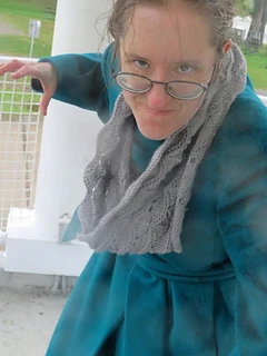 [Image Description: A woman wearing a grey knit lace cowl in a scalloped lace pattern.  The woman is pretending to threaten the camera. ]