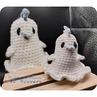 Two crochet ghost chickens in the style of bed sheet ghosts. Their bodies are completely white. They have grey combs, beaks and wattles, and black eyes. One is three times the size of the other.