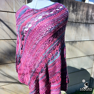 Self-striping yarn crochet poncho photographed outdoors in golden sunlight highlighting the rich stitch texture and flowing color changes.