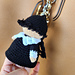 Crochet Wednesday Addams keychain pattern listing photo showing the finished mini doll hanging from a beige bag
