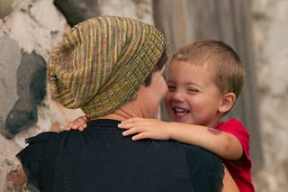 View of a woman with short hair from behind wearing a stripey knit slouch hat and holding a boy toddler who is laughing.
