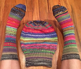 A multi-coloured Sockhead hat lying flat on a wood floor with matching socks on either side.