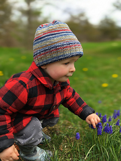 Toddler boy outside wearing a striped knit hat and wearing a red, buffalo plaid jacket.