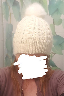 woman whose face has been blocked out wearing a white cable knit hat