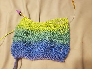 A dishcloth-sized amount of the knitted scarf. The yarn is purple, blue, dark green and light green