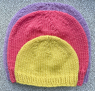 Newborn yellow hat on top of red child's hat on top of purple adult's hat
