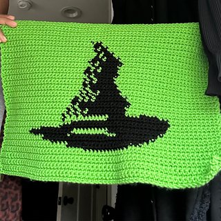 Green and black tapestry features the image of a witch hat