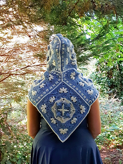 Woman wearing blue and grey crocheted fancy granny square hood in woodland setting (hood up/back view)