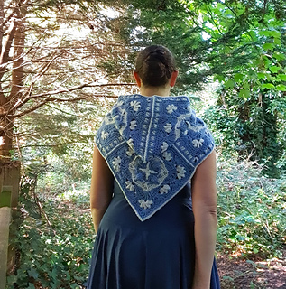 Woman wearing blue and grey crocheted fancy granny square hood in woodland setting (hood down/back view)