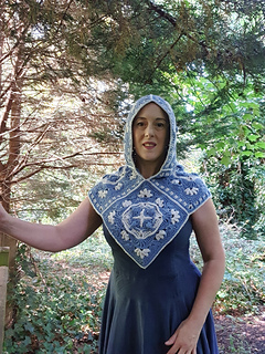 Woman wearing blue and grey crocheted fancy granny square hood in woodland setting (hood up/front view)
