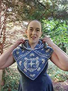 Woman wearing blue and grey crocheted fancy granny square hood in woodland setting (hood down/front view)