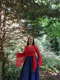 Smiling woman in coral crochet lace wrap cardigan tied at each hip forest holding the ties