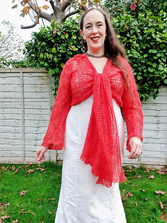 Smiling woman in coral crochet lace wrap cardigan knitted at centre chest walks in a garden 