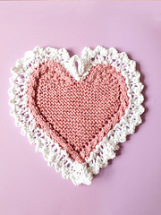 Heart-shaped knitted cloth with white lace edges on a pink background
