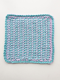 Tunisian crocheted square cloth with hanging loop, worked in a turquoise and lavender pattern on a white background.