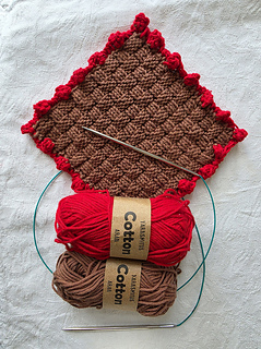 Brown basketweave knitted square with red bobble border and matching yarns