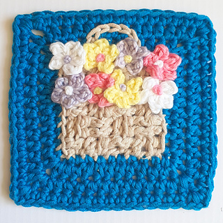 Crocheted square with a beige basket full of colourful flowers on a teal background. 
