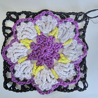 crocheted lilac and violet flower coaster with green detail and black edging 