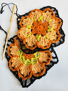 crocheted peach and orangeflower coaster with green detail and black edging