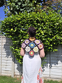 Black lace triangular shawl with bright floral granny squares seen worn from rear