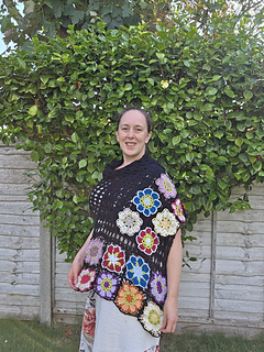 Black lace rectangular shawl with bright floral granny square border at short ends worn wrapped over shoulder